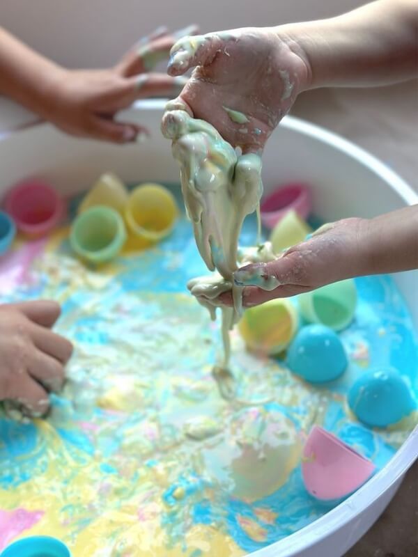 Bowl-containing-oobleck-in-different-colors-plastic-eggs-and-children's-hand-playing-with-the-oobleck-in-fun-Easter-STEM-activities-for-kids. 