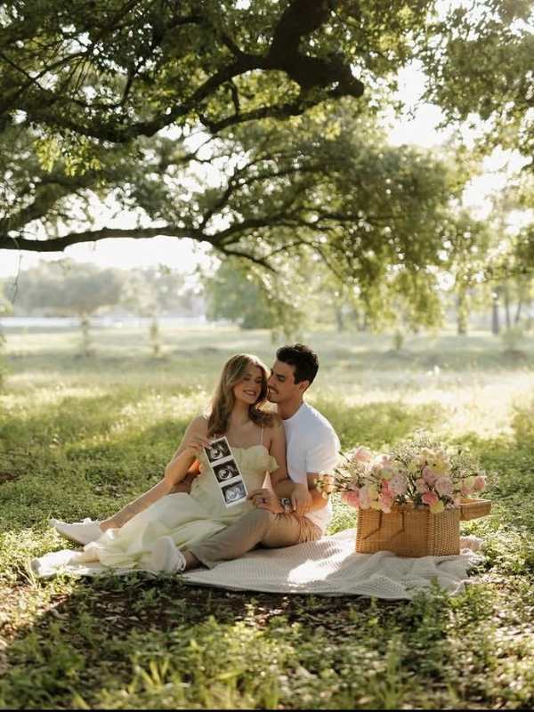 Husband-and-wife-on-a-mat-under-the-tree-with-ultrasound-picture-in-their-hand-and-a-basket-of-flower-beside-them.