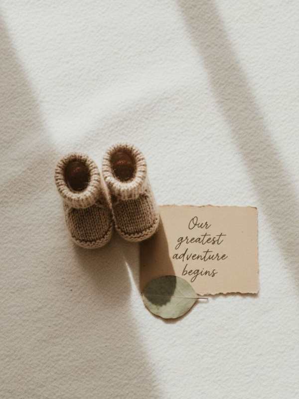 Baby-shoes-with-brown-paper-written-our-greatest-adventure-begins.
