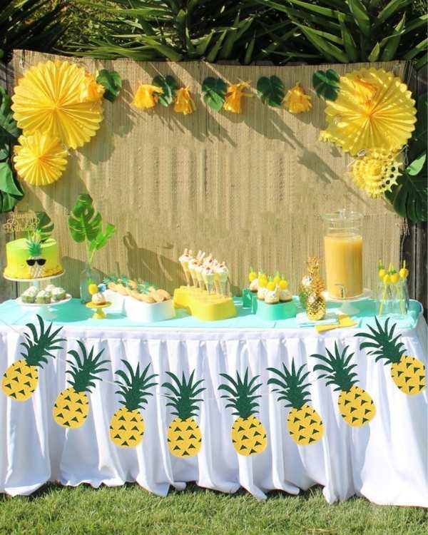 table-with-white-cloth-with-pineapple-printed-on-it-with-other-yellow-and-white-decorations-in-cute-and-affordable-tropical-baby-shower-theme-ideas.