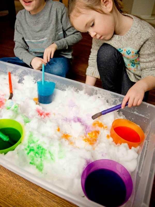 Two-kids-painting-snow-in-a-tray-with-red-blue-green-and-orange-colors.