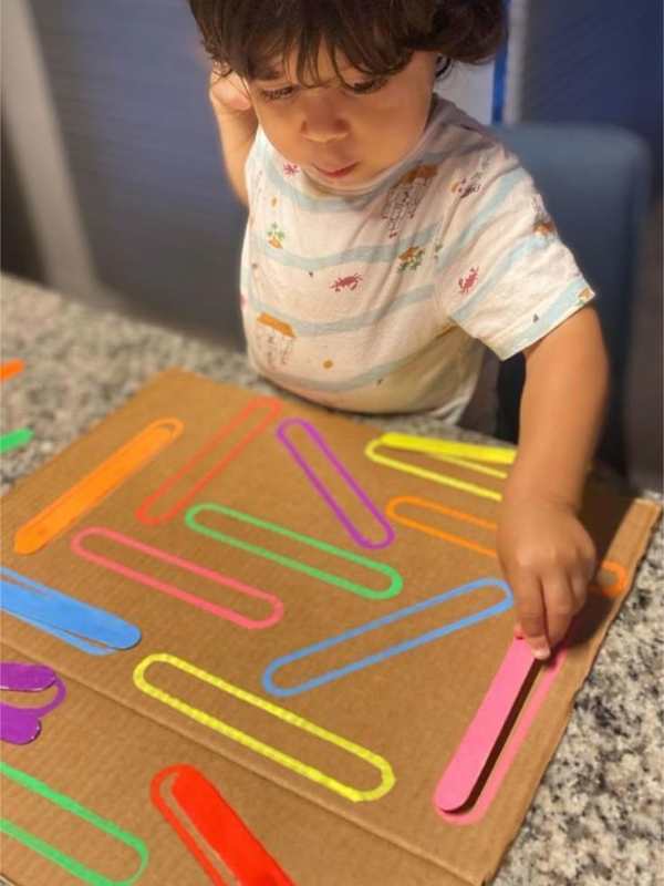 Toddler-matching-colored-popsicle-stick-to-a-corresponding-oval-coloed-shapes-on-paper-in-popsicle-stick-matching-activities-for-toddlers.