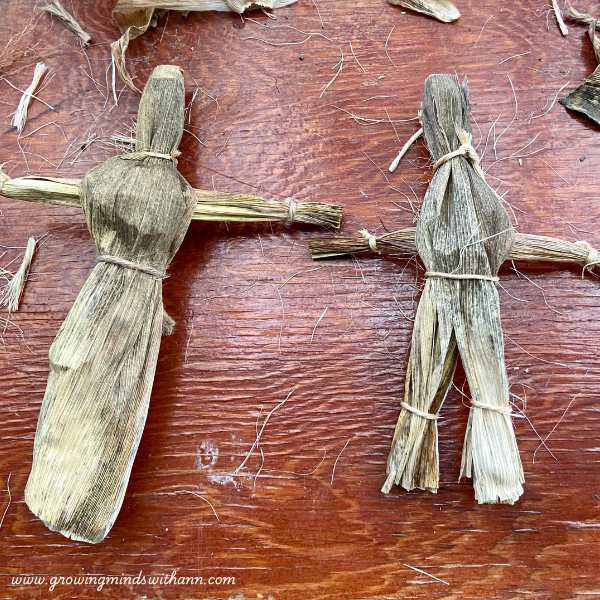Two-corn-husk-dolls-on-a-brown-surface.