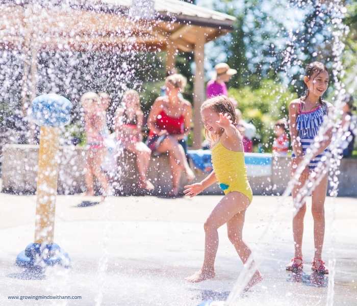 Kids-playing-in-a-splash-pad-with-adults-behind-them-in-summer-bucket-list-ideas-for-families.