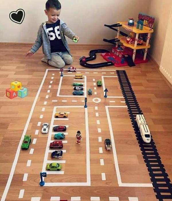Toddler-playing-in-a-tape-road-toy-for-cars-with-toy-cars-parked-inside-it-in-masking-tape-activities-for-toddlers-that-are-easy-and-fun.