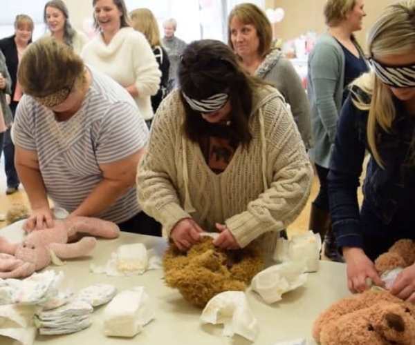 Women-wearing-dolls-diaper-while-being0blindfolded-in-funny-baby-shower-games.
