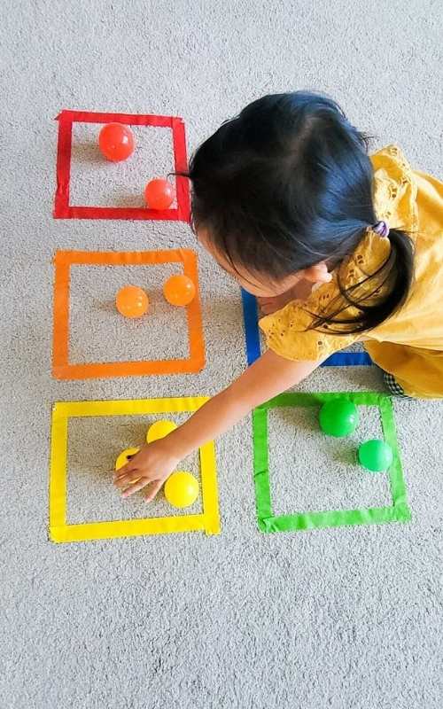 Toddler-sorting-colors-of-small-balls-into-their-colored-space.