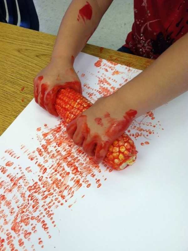 A-kid-hand-rolling-corn-cob-soaked-in-paint-on-a-white-paper-in-harvest-craft-ideas-for-kids-that-are-easy-and-fun.