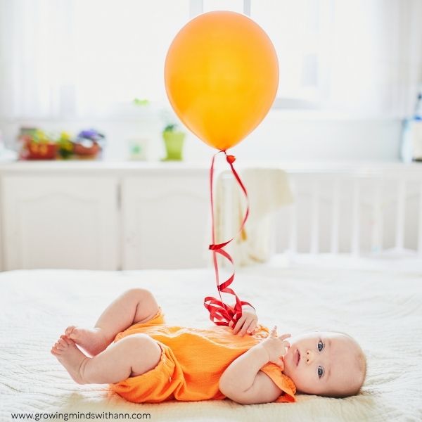 Baby-lying-down-while-holding-a-ribbon-tied-to-a-balloon.