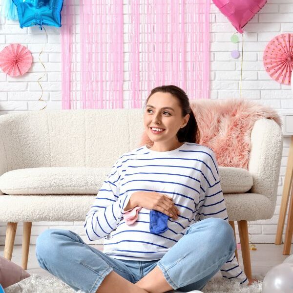 Mom-sitting-on-the-floor-while-holding-blue-and-pink-socks-in-gender-reveal-outfit-ideas-for-mom-to-be.