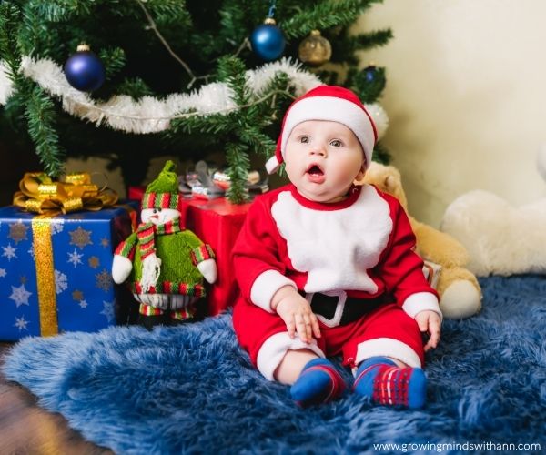 Baby-dressed-in-Christmas-clothes-sitting-beside-a-Christmas-tree.