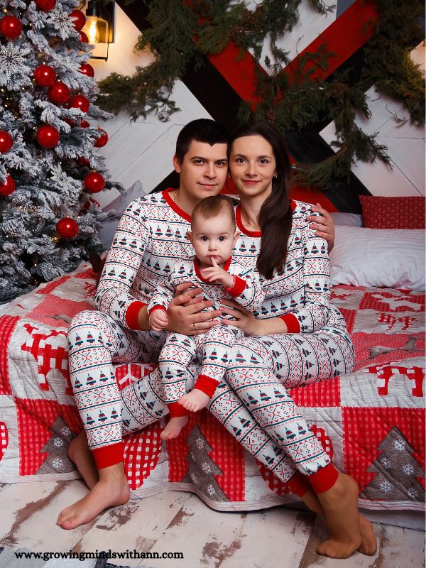 Mom-dad-and-baby-wearing-Christmas-pajamas-sitting-close-to-a-Christmas-tree-in-Christmas-traitions-to-start-with-your-baby.