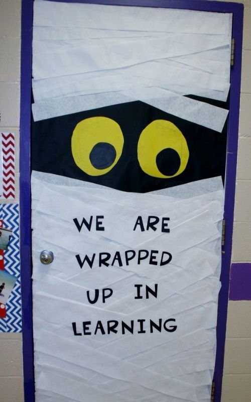 Door-wrapped-in-white-paper-written-we-are-wrapped-up-learning-in-Halloween-classroom-decoration-ideas.